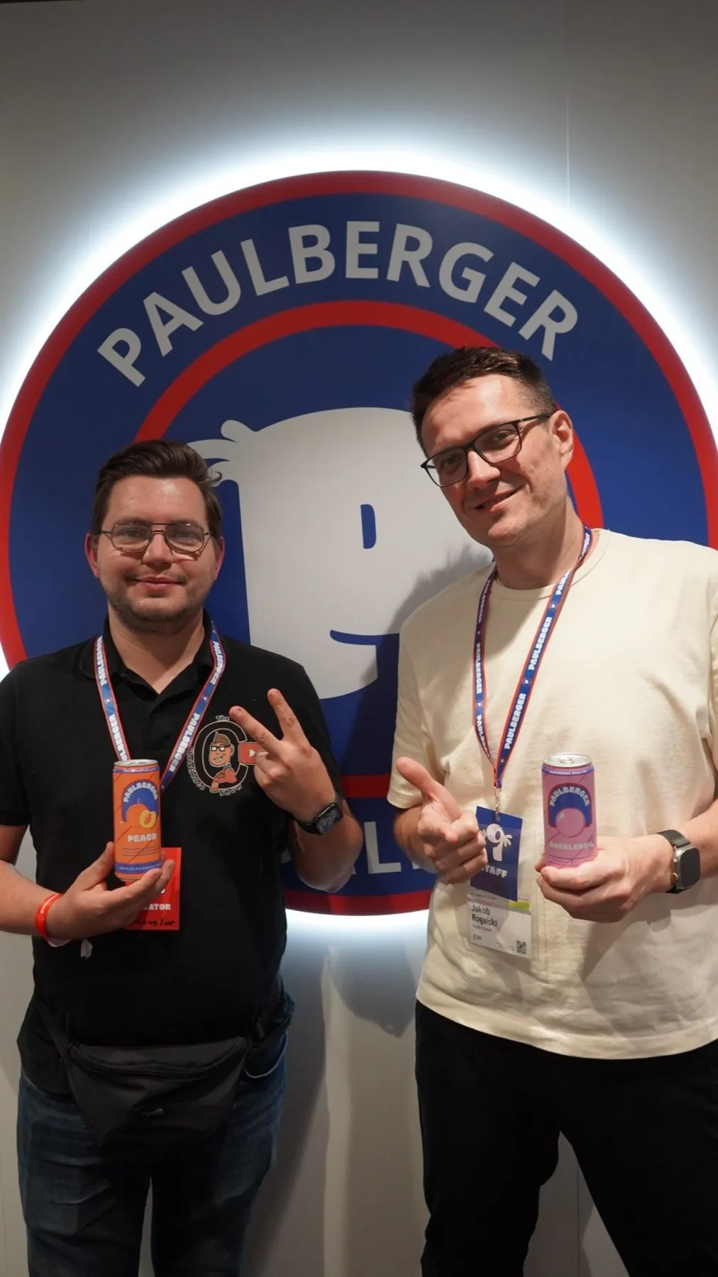 Zwei Männer mit Getränkedosen vor dem beleuchteten Paulberger-Logo